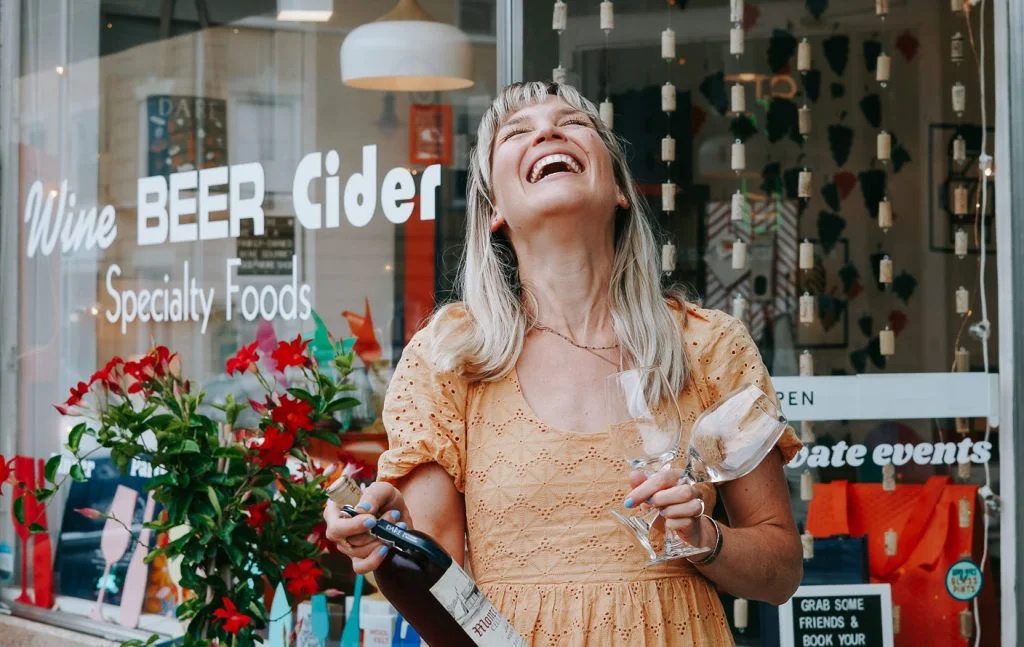 A photo of a lady with her head back laughing and holding a bottle of wine. She is representing the feeling of being free after working with Mungy, a Digital Marketing Agency